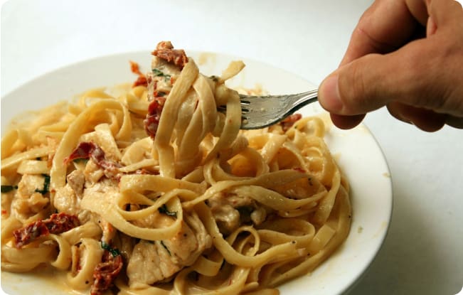 A person is eating pasta with meat and vegetables.