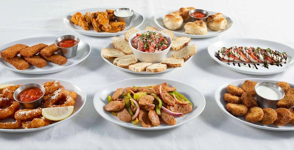 A table filled with plates of food on top of a white cloth.