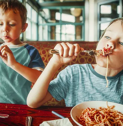 Two children eating spaghetti at a restaurant.