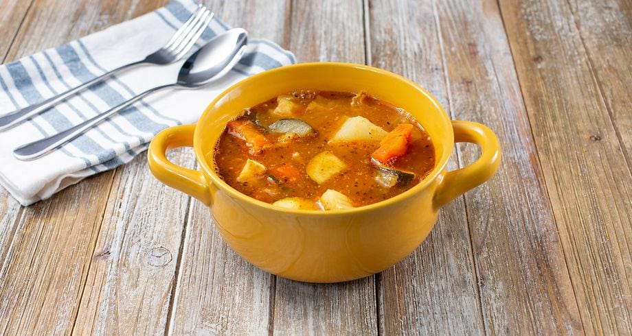 A yellow bowl of soup on top of a wooden table.