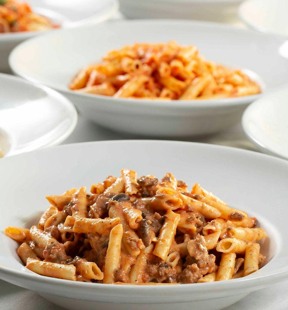 A white bowl filled with pasta and meat.