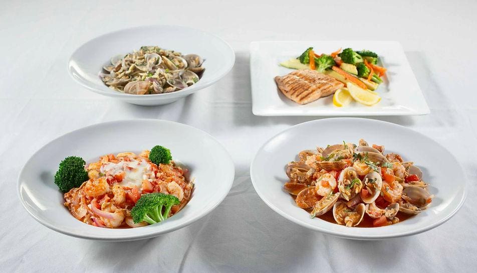 Four bowls of food on a table with plates.