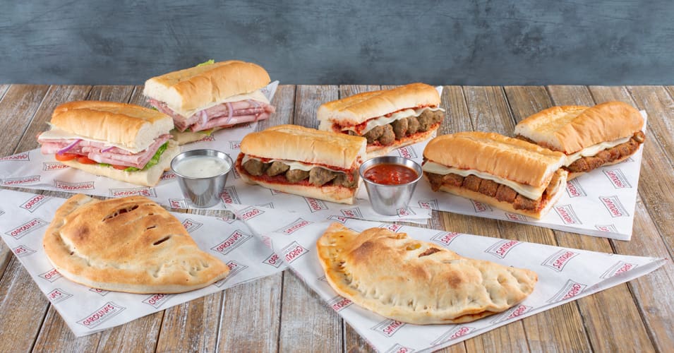 A table topped with sandwiches and cups of sauce.